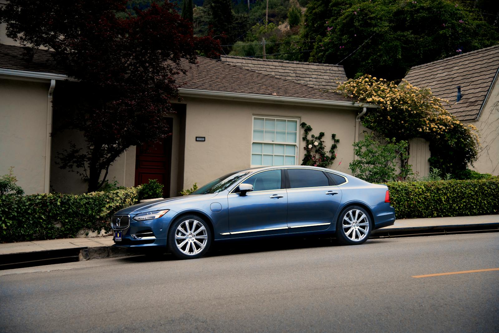 A sleek blue luxury car parked in front of a suburban house with greenery.